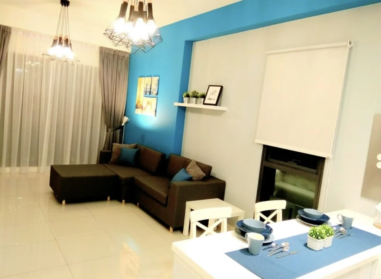 Living features: L-shape sectional sofa in dark grey, blue accent wall, light grey painted walls, white ceiling, hanging pendant lights, floor-to-ceiling sheer curtains, white dining table, white dining chairs, decorative shelf with potted plants, area rug, table setting with blue table runner, wall-mounted artwork; style: modern.